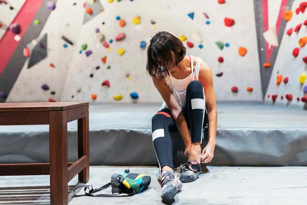 woman putting climbing shoes on for bouldering indoors