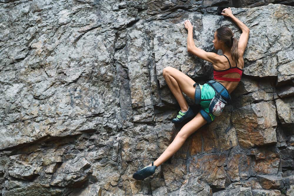 young thin woman climbs on rock outdoors